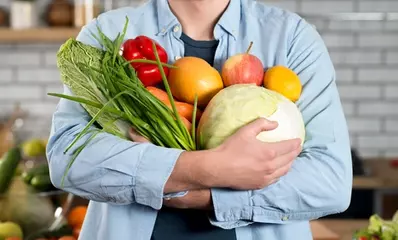 мужчина держит перед собой овощи и фрукты